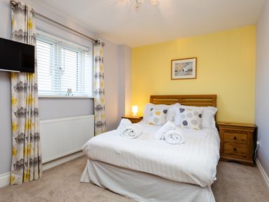 A bedroom with a bed with towels and pillows a window with curtains and a wall mounted television at Harbour Lights House in Seahouses