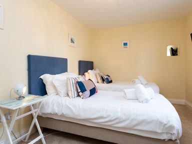 A bedroom with two single beds white bedding blue headboards and a small side table with a lamp at Harbour Lights House in Seahouses