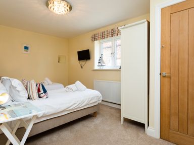 A bedroom with two single beds a wardrobe a wall-mounted tv and a wooden door at Harbour Lights House in Seahouses