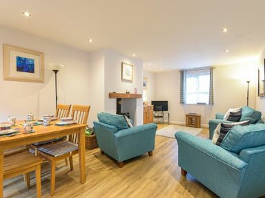 A living room with blue sofas a dining table with chairs a television and a window with curtains at Braidcarr Cottage in Seahouses