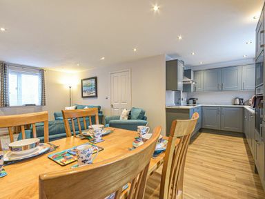 An open plan kitchen and dining area with wooden dining table and chairs blue sofas and grey kitchen cabinets at Braidcarr Cottage in Seahouses
