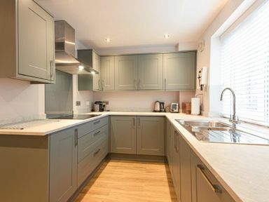 A kitchen with grey cabinets a stainless steel sink a stove and small appliances on countertops at Braidcarr Cottage in Seahouses