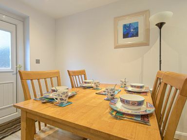 A dining table set with four place settings including bowls mugs and cutlery in a room with wooden chairs a lamp and a framed picture on the wall at Braidcarr Cottage in Seahouses