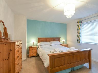 A bedroom with a wooden bed and dresser bedside tables with lamps and a window with blinds and curtains at Braidcarr Cottage in Seahouses