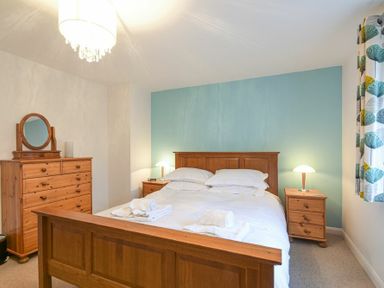 A bedroom with a wooden bed and bedside tables against a blue accent wall at Braidcarr Cottage in Seahouses