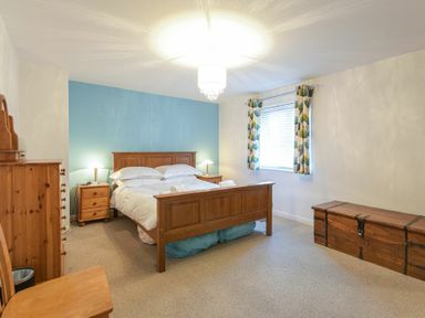 A bedroom with a wooden bed chest of drawers chair and window with patterned curtains at Braidcarr Cottage in Seahouses