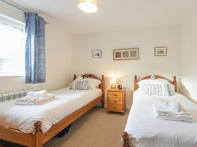 A bedroom with two single beds a wooden nightstand with a lamp and three framed pictures on the wall at Braidcarr Cottage in Seahouses