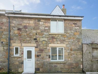 Exterior view of a stone cottage with white door and two windows at Braidcarr Cottage in Seahouses