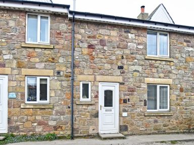 A stone exterior wall of a house with white doors and windows at Braidcarr Cottage in Seahouses