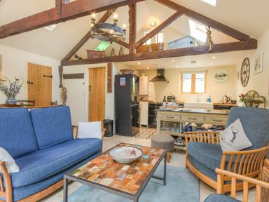 A living room with blue sofas a wooden coffee table and an open kitchen at The Byre at Warkworth