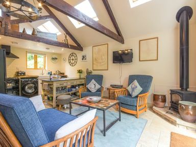 A seating area with blue armchairs and a coffee table next to a kitchen and wood burning stove at The Byre at Warkworth