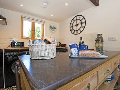 A kitchen with a black countertop island holding a wicker basket and blue tea set with bread at The Byre at Warkworth in Warkworth