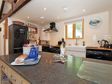 A kitchen with black refrigerator wooden shelves white farmhouse sink and a kitchen island at The Byre at Warkworth