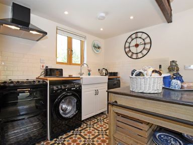 A kitchen with a stove washing machine sink and island with basket at The Byre at Warkworth