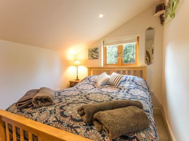 A bedroom with a wooden bed a patterned bedspread pillows towels a bedside table with lamp and a window at The Byre at Warkworth in Warkworth
