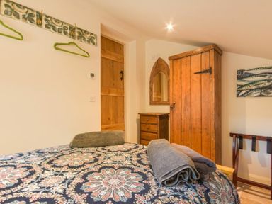 A bedroom with a bed covered in patterned bedding with towels on top a wooden wardrobe a small wooden chest of drawers and a wooden door at The Byre at Warkworth in Warkworth