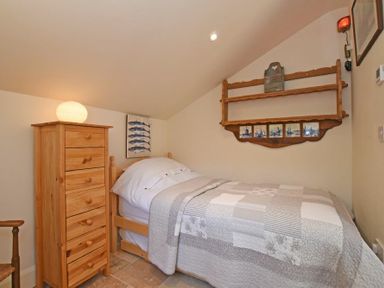 A small bedroom with a single bed with gray and white quilt a wooden chest of drawers and a wooden wall shelf at The Byre at Warkworth in Warkworth