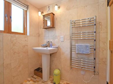 A bathroom with a pedestal sink wooden mirror cabinet towel rack and a window at The Byre at Warkworth