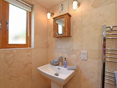 A bathroom with a sink a wall mirror a window and a towel rail at The Byre at Warkworth