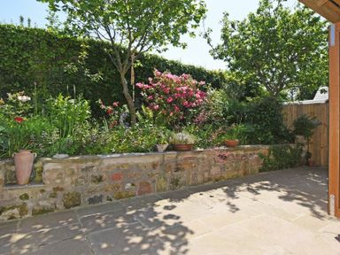 A garden with flowers trees and stone wall next to a paved patio at The Byre at Warkworth in Warkworth