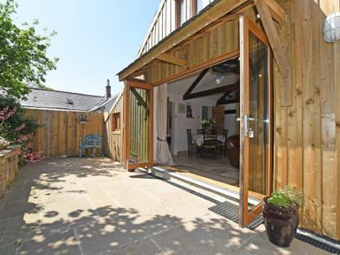 An outdoor patio area with tiled floor and wooden fence with open wooden framed glass doors leading to a dining area at The Byre at Warkworth