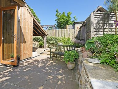 An outdoor patio with stone flooring a wooden bench potted plants a wooden shed and a wooden fence at The Byre at Warkworth in Warkworth