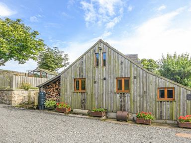 A wooden building with small windows and flower boxes along a gravel path at The Byre at Warkworth