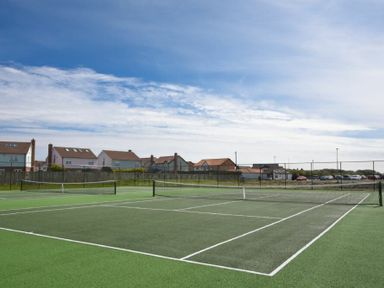 An outdoor tennis court with nets and houses in the background at Spindrifter in Beadnell