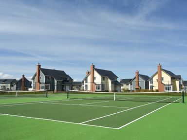 A tennis court in front of multiple two story houses at Spindrifter in Beadnell