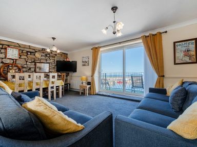 A living room with blue sofas a dining table and sliding glass doors leading to a balcony at Lobster Lodge in Seahouses