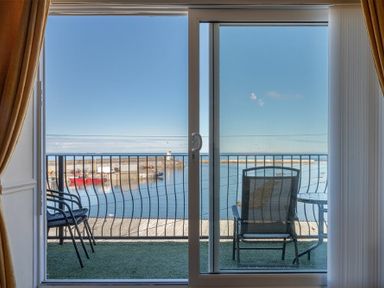 View through sliding glass doors to a balcony with chairs and table overlooking a harbor at Lobster Lodge in Seahouses