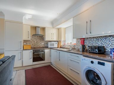 A kitchen with white cabinets mosaic tile backsplash and appliances at Lobster Lodge in Seahouses