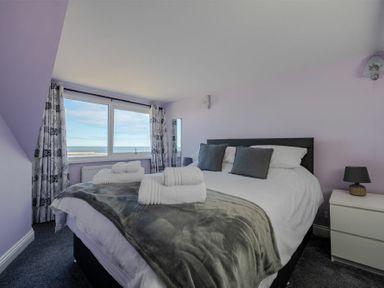 A bedroom with a bed covered with white bedding grey pillows and towels folded on top and a window with patterned curtains at Lobster Lodge in Seahouses