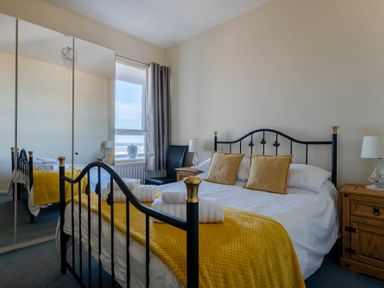 A bedroom with a black metal bed frame yellow blankets mirrored closet doors and wooden bedside cabinets at Lobster Lodge in Seahouses