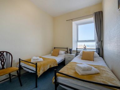 A bedroom with two single beds a window with curtains a chair and a nightstand at Lobster Lodge in Seahouses