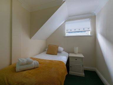 A small bedroom with a single bed with yellow bedding a nightstand with a lamp and a window with a roller blind at Lobster Lodge in Seahouses