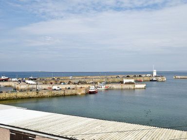 A harbor with boats docked and vehicles on the pier at Lobster Lodge in Seahouses