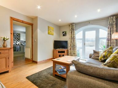 A living room with a sofa wooden coffee table television and an open doorway to a kitchen at East Havers in Alnwick