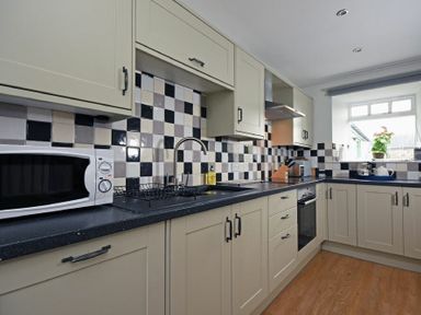 A kitchen with beige cabinets a microwave oven dish rack stove oven and window with plant at East Havers in Alnwick