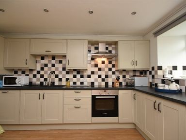 A kitchen with cream cabinets black and white checkered backsplash stove microwave and various kitchen appliances at East Havers in Alnwick