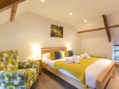 A bedroom with a wooden bed with yellow and black pillows and a green patterned armchair at East Havers in Alnwick