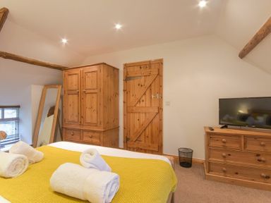 A bedroom with a bed covered in a yellow blanket and white towels with wooden furniture including a wardrobe dresser and a door at East Havers in Alnwick