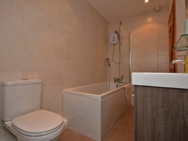 A bathroom with a toilet a bathtub with shower and a sink with wooden cabinetry at East Havers in Alnwick