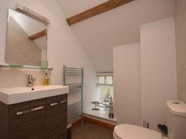 A bathroom with a sink cabinet, mirror, towel rack, toilet, and decorative items on a window sill at East Havers in Alnwick