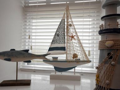 A decorative model fish sailboat and lighthouse in front of a window with blinds at East Havers in Alnwick