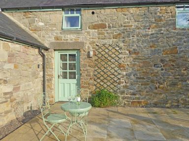 A stone patio with a metal table and two chairs and a door leading to a stone building at East Havers in Alnwick