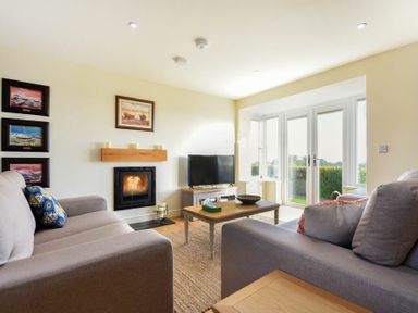 A living room with two sofas a coffee table a TV and a fireplace near glass doors at Rock Lodge in Alnmouth