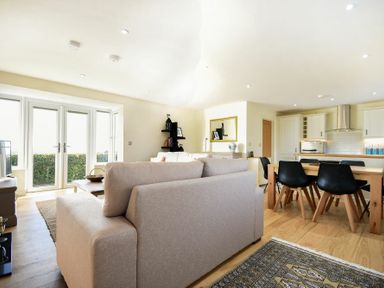 A living room with sofas a dining table and chairs next to a kitchen with white cabinets at Rock Lodge in Alnmouth