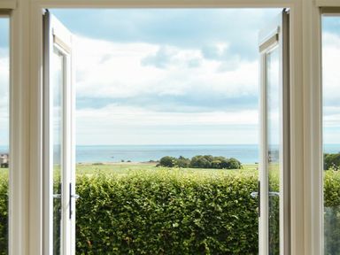 A view through open doors showing a hedge green fields trees and the sea at Rock Lodge in Alnmouth