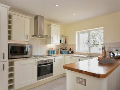 A kitchen with white cabinets a microwave an oven a stovetop and a wooden countertop at Rock Lodge in Alnmouth